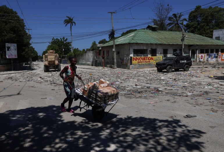 A woman pushes a wheelbarrow past security forces in Haiti's Port-au-Prince