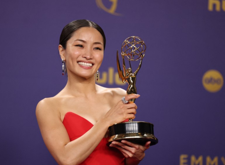 Anna Sawai holding her Emmy. She is wearing a red evening gown. She is smiling.