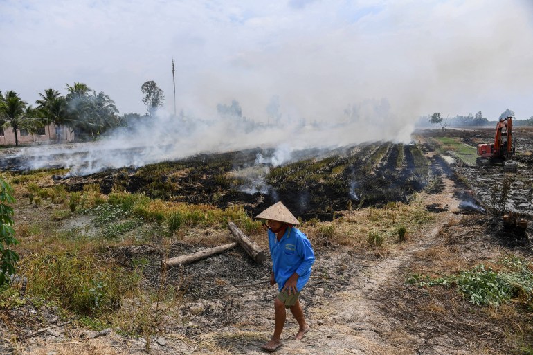 This photo taken on February 28, 2023 shows a farmer walking past burning straw stubble in a rice field in Can Tho. Rice -- Asia's principal staple -- is to blame for around 10 percent of global emissions of methane, a gas that over two decades traps about 80 times as much heat as carbon dioxide. (Photo by Nhac NGUYEN / AFP) / TO GO WITH "VIETNAM-CLIMATE-METHANE-RICE,FOCUS' BY TRAN TRI MINH HA AND ALICE PHILIPSON - To go with "VIETNAM-CLIMATE-METHANE-RICE,FOCUS' by Tran Tri Minh Ha and Alice Philipson