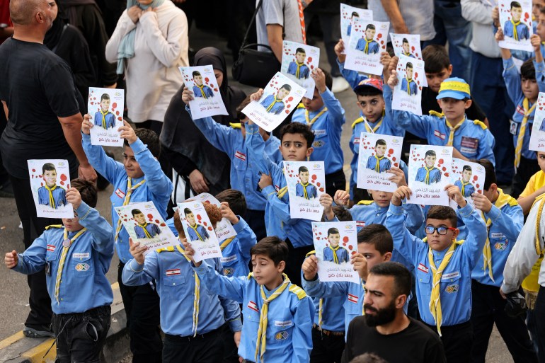 Boy scouts raise the picture of a fellow scout, killed when hundreds of paging devices exploded in a deadly wave across Lebanon the previous day, during the funeral procession of some of those killed, in Beirut's southern suburbs on September 18, 2024. - Hundreds of pagers used by Hezbollah members exploded across Lebanon on September 17, killing at least nine people and wounding around 2,800 in blasts the Iran-backed militant group blamed on Israel. (Photo by ANWAR AMRO / AFP)