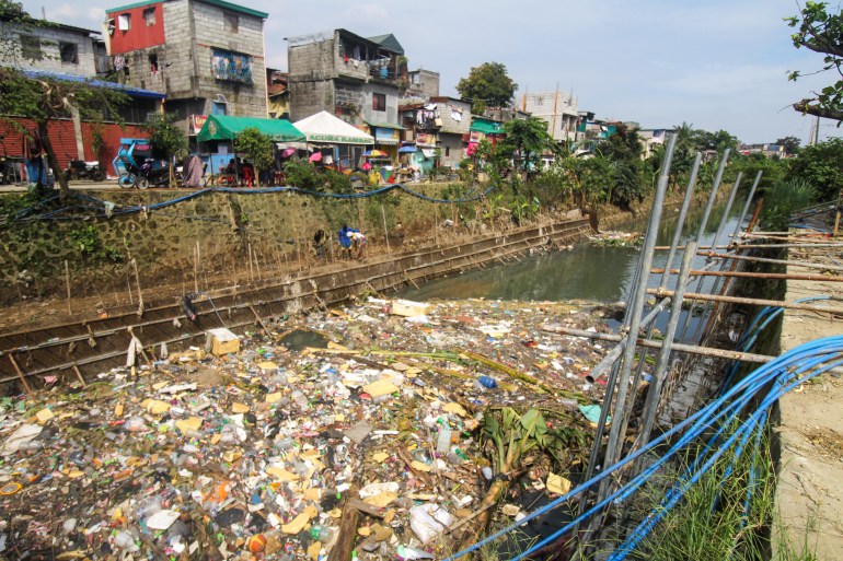 Rubbish piled up along a creek in a Manila neighbourhood. There are rows of small houses next to the creek