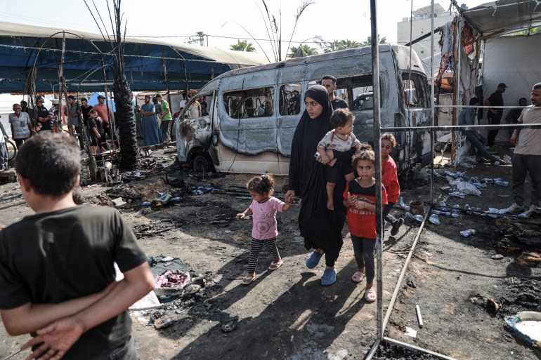 Madi walking with her chidlren through the destruction caused by Israel bombing a displacement camp in the curtyard of Al-Aqsa Martyr's Hospital