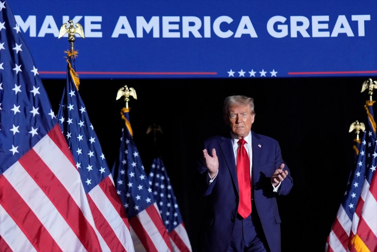 Donald Trump claps at a rally, as he walks past a row of US flags under a "Make America Great Again" sign.