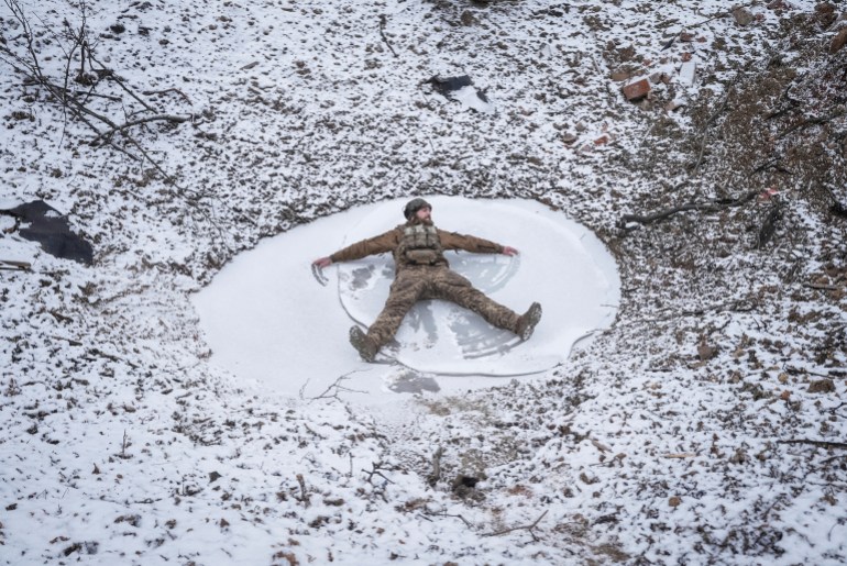 A Ukrainian serviceman of 80th Separate Galician Air Assault Brigade makes a snow angel in a bomb crater, amid Russia's attack on Ukraine, at a position near Bakhmut in Donetsk region, Ukraine January 25, 2024. REUTERS/Inna Varenytsia TPX IMAGES OF THE DAY