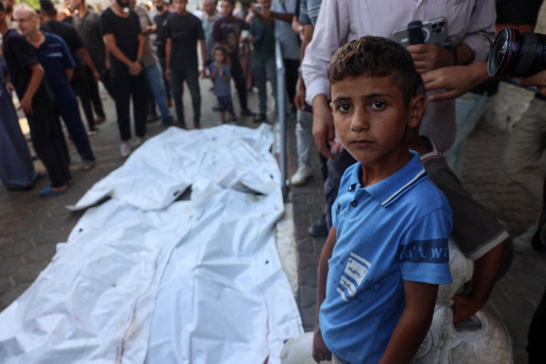 A boy stands with others near the bodies of people killed in a house hit by an Israeli strike, in the courtyard of a hospital in Deir El-Balah the central Gaza Strip on October 4