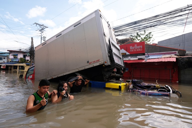 People wade through a flooded road brought about by Tropical Storm Trami, in Naga, Camarines Sur on October 25, 2024. Philippine rescue workers battled floodwaters on October 25 to reach residents still trapped on the roofs of their homes as Tropical Storm Trami moved out to sea after killing at least 40 people. (Photo by ZALRIAN SAYAT / AFP)