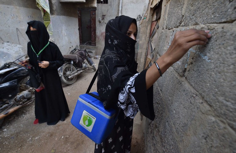 Health workers mark locations as they administer polio vaccines to children during a door-to-door vaccination campaign in Karachi