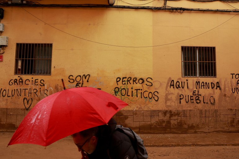 A man walks past graffiti reading "Thanks volunteers. Politician dogs, the people rule here", following catastrophic flooding, as Spain braces for more torrential rain, in Paiporta, Valencia, Spain November 13, 2024. REUTERS/Vincent West