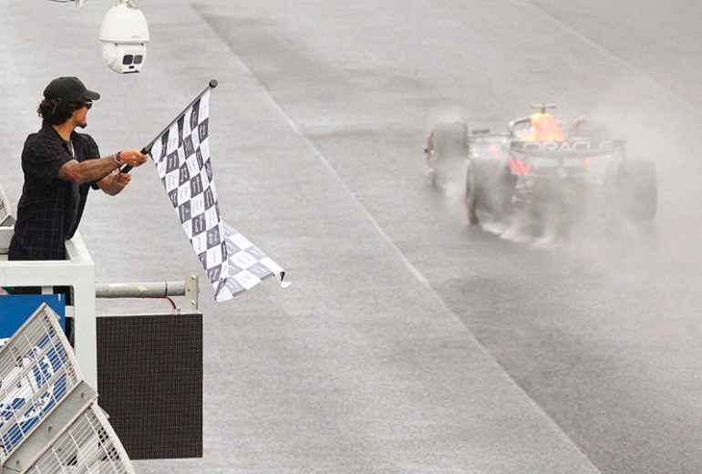 Brazilian surfer Gabriel Medina waves the chequered flag to Red Bull Racing's Dutch driver Max Verstappen after winning the Formula One Sao Paulo Grand Prix, at the Jose Carlos Pace racetrack, aka Interlagos, in Sao Paulo, Brazil, on November 3, 2024. (Photo by Sebastiao Moreira / POOL / AFP)