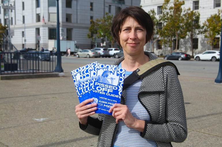 A woman holds up copies of the Pissed Off Voter Guide in front of San Francisco City Hall