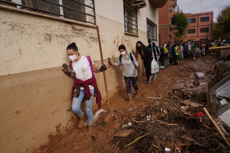 Volunteers walk in the mud to help with the clean up operation after floods in Massanassa, just outside of Valencia, Spain, Saturday, November 2, 2024. [AP Photo/Alberto Saiz]