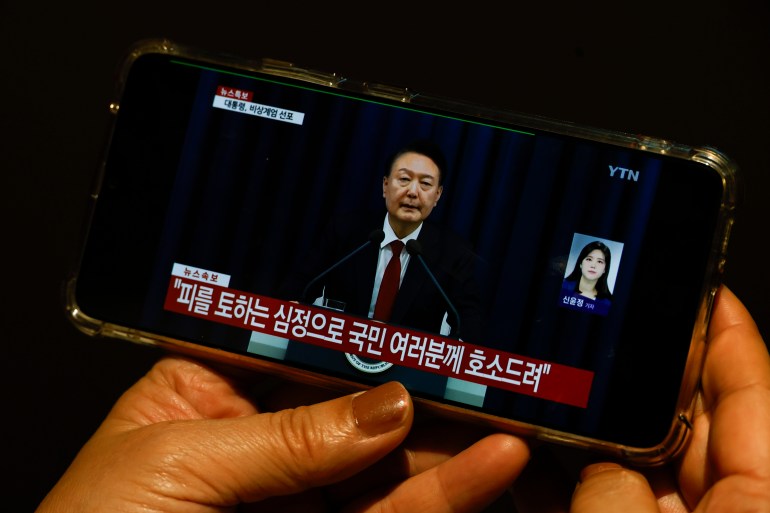 A South Korean tourist watches a Japanese TV broadcast on a phone showing South Korean President Yoon Suk Yeol 