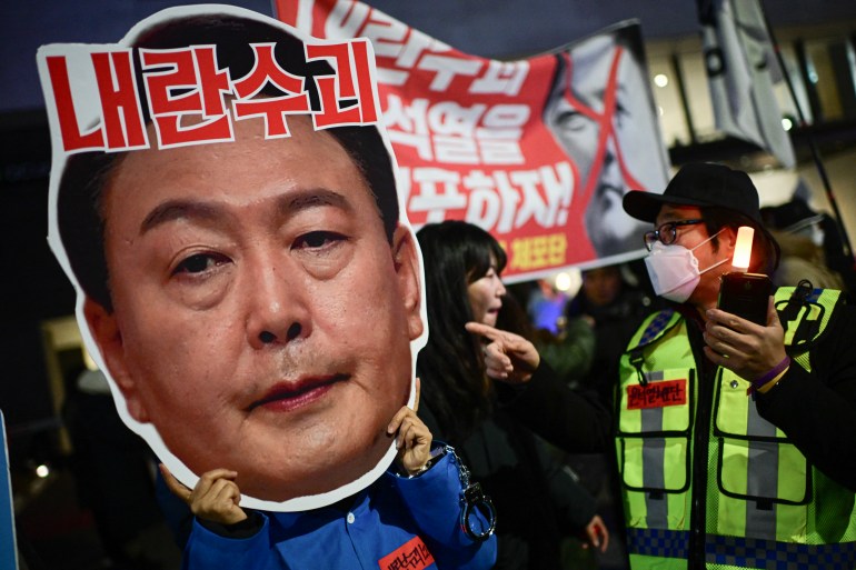 A protester holding a cardboard reading "Leader of insurgents" on an image depicting the face of South Korea's President Yoon Suk Yeol