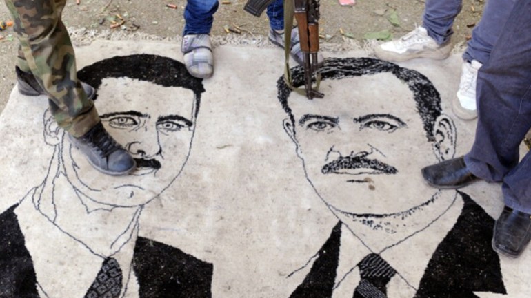 Syrian opposition fighters standing on a mat bearing drawings of Syrian President Bashar al-Assad and his late father Hafez [AFP]