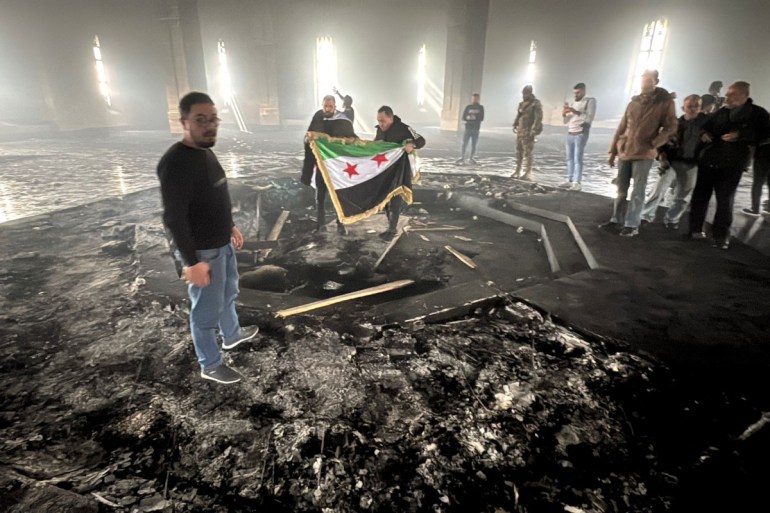 Rebel fighters stand with the flag of the revolution on the burnt gravesite of Syria's late president Hafez al-Assad at his mausoleum in the family's ancestral village of Qardaha