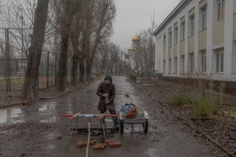 a man stands with a water bottle next to a cart in a wintry street